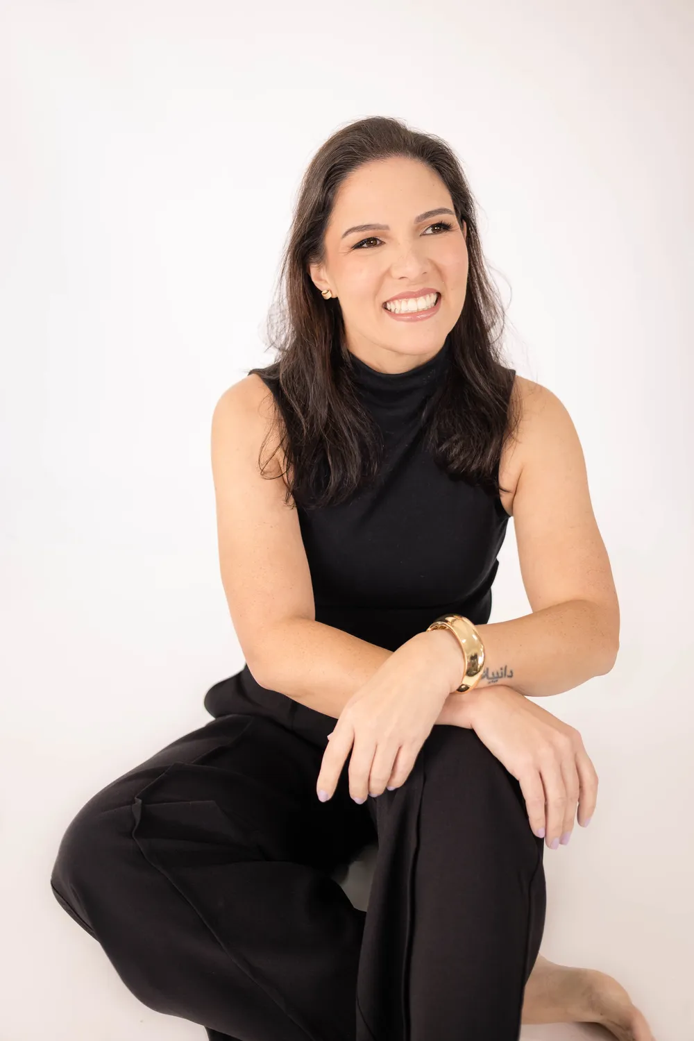 Retrato profissional de Daniela Sotilo sorrindo, sentada, em fundo claro de estúdio
