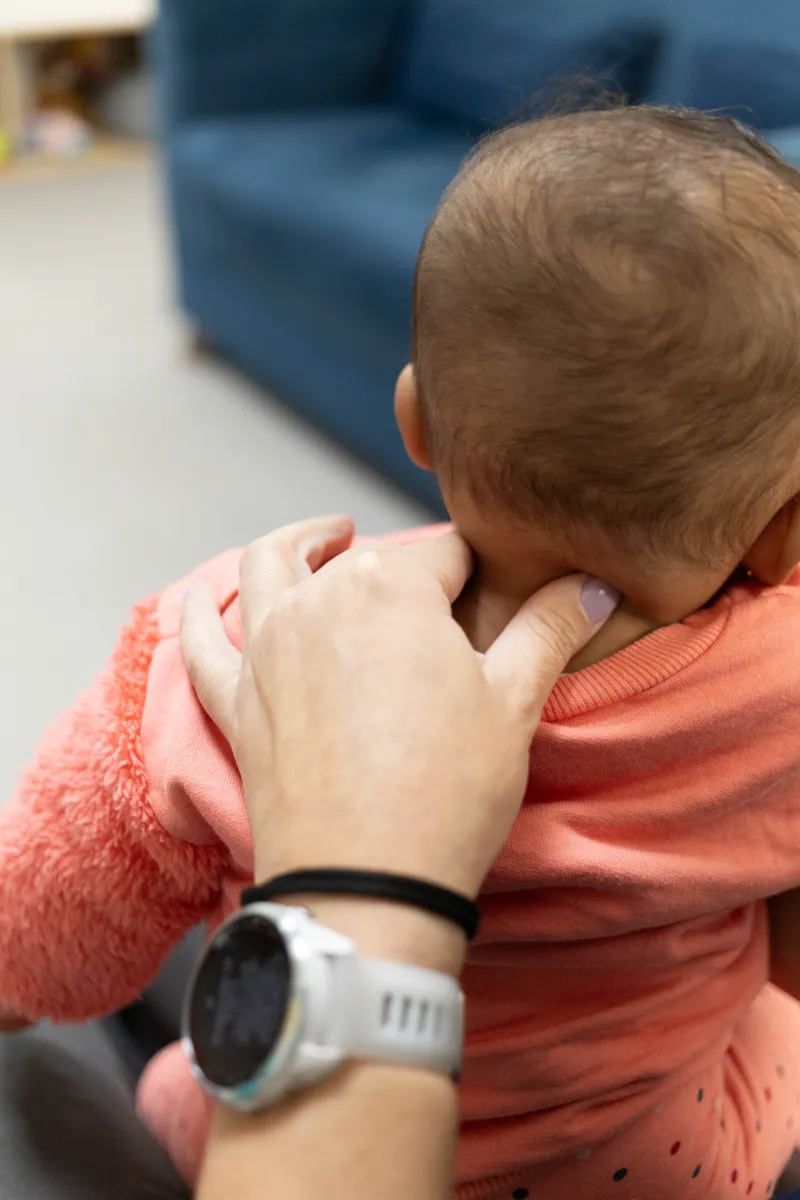 Mãos da fisioterapeuta palpando a região cervical de um bebê durante atendimento